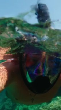 Maskeli adam denizdeki su yüzeyinde yüzüyor. Suya tekrar ve tekrar bakın. Dikey Video