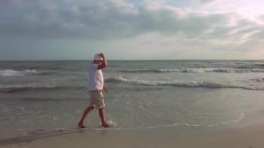 Görüntülerde, sıcak yaz akşamı güneşi altında dalgaların bacaklarına hafifçe vurduğu deniz kenarında gezinen bir adam görülüyor.