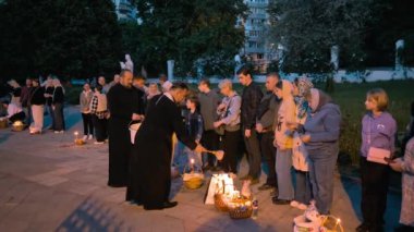 Kyiv, Ukraine - May 4, 2024: A priest sprinkles water on people standing outside the Pokrovskaya Church in Kyiv on Easter Eve to consecrate baskets of baked goods and Easter eggs, according to Orthodox Christian tradition. 