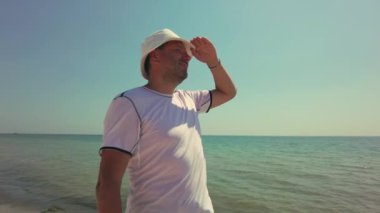 Adam sahilde duruyor, huzurlu okyanus manzarası ve tatilinin tadını çıkarırken, yaz akşamının güzelliğini alıyor.