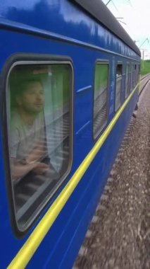 Adam trenin penceresinden manzaralı bir ortam alıyor, sonra da tahmini varış zamanını kontrol etmek için saatine bakıyor.