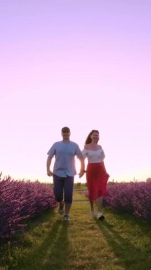 Sabahın erken saatlerinde, bir çift yeni bir günün başlangıcını kutlamak için lavanta denizinde birlikte koşar. Ağır çekim. Dikey Video