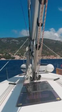 Güneşli bir yaz gününde, bir yelkenli yatı sahildeki manzaralı bir limana doğru yol alıyor. Bakış açısı. Dikey Video