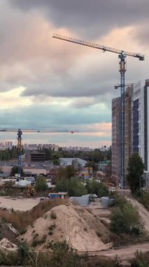 Vinçler gün batımında yorulmadan bir inşaat sahasında çalışırlar. Bulutlar üstlerinden geçerken onları hızlandırır ve insan gelişimi ile doğal güzelliğin karışımını vurgularlar. Zaman atlaması. Dikey Video