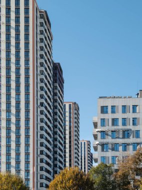 Açık mavi gökyüzünün arkaplanına karşı bu apartmanlar, sakin sonbahar mevsiminde şehir hayatının özünü somutlaştıran uzun binalar..