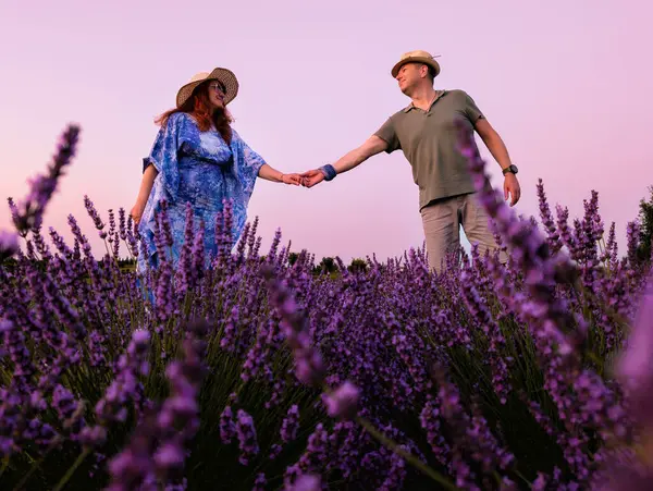 Lavanta tarlasında eğlenen bir çift fotoğraf için poz veriyor ve el ele tutuşuyor.