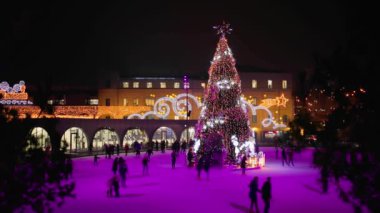 Noel 'in büyüsü buz pateni sahasında parlıyor. İnsanlar aydınlatılmış tatil ışıkları altında paten kayarken geceyi şenlikli neşeyle dolduruyor.