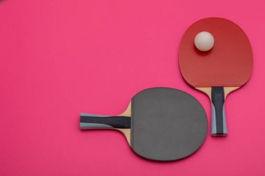 Siyah ve kırmızı pinpon raketlerinin yer aldığı minimalist kompozisyon rekabet kalitesinde beyaz top, çağdaş spor estetiği için canlı pembe arka plana karşı tasarlandı