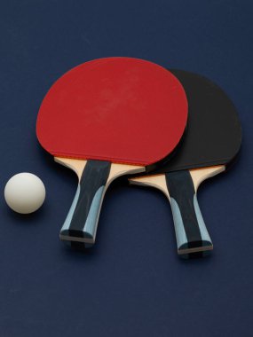 Profesyonel düzeydeki pinpon raketlerinin zarif kompozisyonu canlı kırmızı ve siyah kauçuk yüzeyli, derin donanma arka planında şekillendirilmiş.