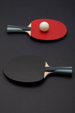 Turnuva düzeyinde bir masa tenisi raketinin stil olarak köşegen çekimi. Üzerinde dokulu kırmızı kauçuk yüzey ve mavi aksanlı ergonomik ahşap sapı var. El değmemiş beyaz top ile tamamlanmış.