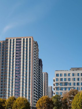 Açık mavi gökyüzünün arkaplanına karşı bu apartmanlar, sakin sonbahar mevsiminde şehir hayatının özünü somutlaştıran uzun binalar.