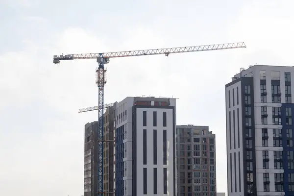 Bir vinç gün boyunca inşaat alanında ayakta duruyor ve inşaat malzemelerini aktif olarak kaldırıyor. İlerleme kaydedildikçe parlak gün ışığı alanı aydınlatıyor.