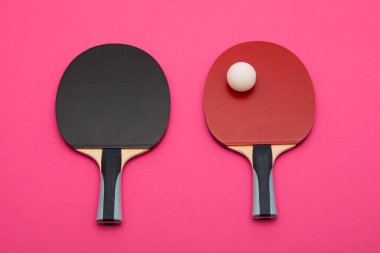 Çağdaş spor tasvirleri için canlı pembe arkaplan karşısında siyah ve kırmızı yüzey ile rakip topun yer aldığı profesyonel pin pon raketleri