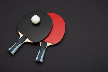 Ahşap saplı siyah ve kırmızı kauçuk yüzeyli iki profesyonel masa tenisi raketinin zarif kompozisyonu, yanında da siyah arka plandaki beyaz top.