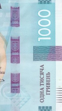 Ulusal üç dişli mızrak amblemi, koruyucu dalga desenleri ve mezhep numarası içeren 1000 UAH banknotunun yakın görüntüsü, gelişmiş güvenlik unsurlarını mavi tonlarda gösteriyor. Dikey Video