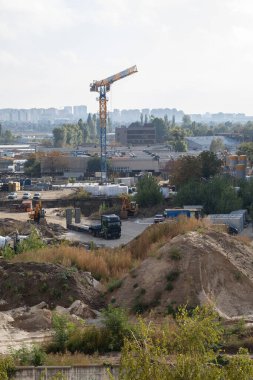 Gün ışığında çalışan büyük bir vinci olan bir inşaat alanı. Sahne, projenin gelişimini gösteren işçiler ve malzemelerle dolu.