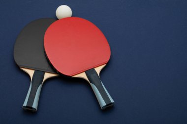 Minimalist kompozisyon: Siyah ve kırmızı renkte pinpon raketleri. Artistik olarak derin donanma arkaplanına yerleştirilmiş, maksimum görsel etki için.