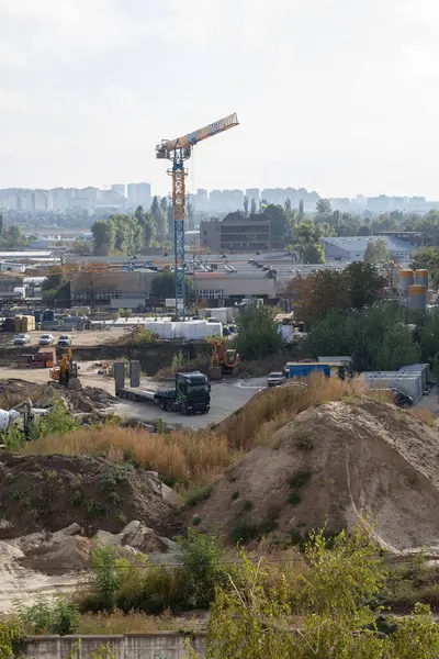 Gün ışığında çalışan büyük bir vinci olan bir inşaat alanı. Sahne, projenin gelişimini gösteren işçiler ve malzemelerle dolu.