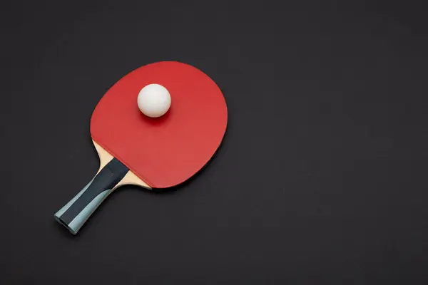 Asgari düzeyde pinpon raketi, canlı kırmızı kauçuk yüzey ve düzenleyici beyaz top, koyu renk zemine karşı birinci sınıf spor ekipmanları sergiliyor.