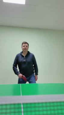Profesyonel masa tenisi teknikleri ve atletik hareketleri dikey formatta sergileyen yetenekli amatör, dinamik servisler sunuyor ve kapalı masa tenisi tesislerinde nane yeşili arka planda mitingler düzenliyor. Dikey Video
