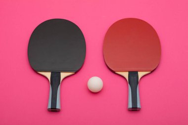 Pembe arka planda modern spor ekipmanları tasarımı üzerine kurulmuş, rekabetçi kalitede beyaz topu olan siyah ve kırmızı ping pong raketleri.