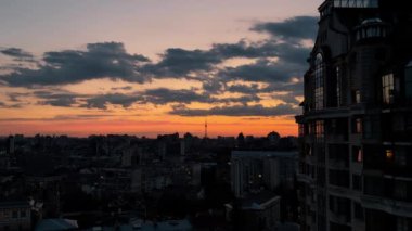 Altın saat boyunca nefes kesen şehir manzarası dramatik turuncu gökyüzüne karşı lüks konut binası. İkonik televizyon kulesi ve şehir siluetleri ile şehir manzarası sıcak gün batımı ışığı ile yıkanmış atmosferik atmosfer yaratıyor, Kyiv, Ukrayna