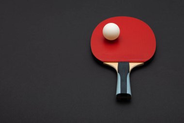 Turnuva derecesinde bir ping pong raketi içeren, kırmızı kauçuk yüzey ve ergonomik ahşap saplı, el değmemiş beyaz top ve siyah arka planla tamamlanmış bir sanat stüdyosu çekimi.