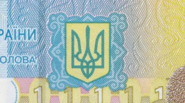 Bir Hryvnia banknotunda yer alan sarı ve mavi mızraklı Ukrayna ulusal ambleminin ayrıntılı yakın plan görüntüsü, koruyucu unsurlar ve eğimli arka planla resmi devlet sembolünü gösteriyor