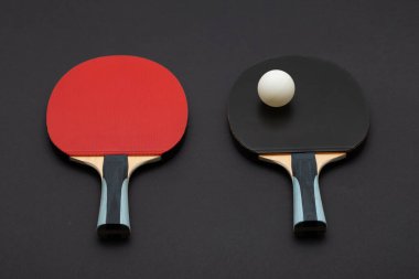 Kırmızı ve siyah kauçuk yüzeyli iki turnuva dereceli ping pong raketinin yer aldığı minimalist stüdyo kompozisyonu, mavi aksanlı ahşap saplar ve beyaz top.