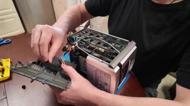 Bir kişi, bir atölye ayarındaki araçları kullanarak iç bileşenlerini ve açık kablolarını kullanarak parçalanmış bir teybi CD çalarla onarmaya çalışır.