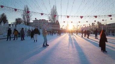 Kyiv, Ukrayna - 14 Şubat 2025: İnsanlar sıcak kış güneşinin altında kayarken kalp şeklinde ışıklarla süslenmiş canlı bir açık hava buz pateni pisti