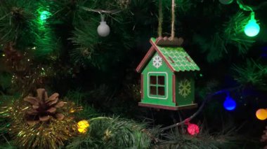 Büyüleyici ahşap bir ev süsü parıldayan ışıklar ve çelenklerle çevrili yeşil bir Noel ağacının dalında asılı duruyor ve çam kozalağı sıcak bir tatil dokunuşu ekliyor. Hitchcock 'un ikonik yakınlaştırma efekti