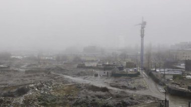 Görünür vinçler ve kentsel çevrelere sahip bulutlu bir gökyüzü altında dinamik hava koşullarını kuru koşullardan sis ve kara dönüştüren bir inşaat alanı.