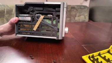Ahşap bir masada parçalanmış bir stereo sistem. Görünür iç bileşenler ve kablolar tamir işlemi sırasında araçlar ve ellerle inceleniyor