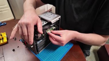  Bir kişi görünür devre kartlarıyla parçalanmış bir elektronik cihazı, soğutma vantilatörü, ısıtıcı ve kabloları atölyedeki bir masada kullanılan aletleri tamir etmeye çalışır.