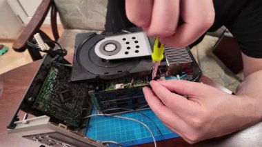 Bir kişi, bir atölyede devre kartı ve elektronik parçaları üzerinde çalışırken CD çalar üzerindeki bir kasetçaları tamir etmek ve sökmek için tornavida kullanır.