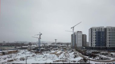 Dinamik zaman çizelgesi, kış koşullarında birden fazla vinç kullanan bir yerleşim tesisinin inşaat sürecini yakalıyor ve karlı bir şehir manzarasına karşı kentsel gelişimi gösteriyor.