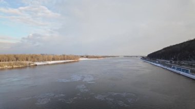  Kyiv 'deki Dnipro Nehri' nin kış manzarası, su yüzeyinde yüzen buz parçaları, bir tarafında karlı bir set, diğer tarafında çıplak ağaçlar bulutlu bir gökyüzünün altında.