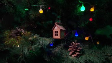 Kar tanesi detaylarıyla süslenmiş kahverengi ahşap bir ev süsü güzel dekore edilmiş bir Noel ağacına asılı renkli ışıklar, çam kozalakları ve şenlikli çelenklerle