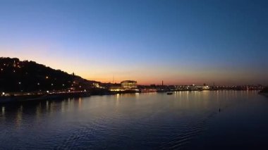 Gün batımında Dinyeper Nehri 'nin nefes kesici zamanlaması su yüzeyindeki altın ufuk yansımaları ve aydınlatılmış kentsel kıyı şeridi ile günden geceye kademeli geçişi yakalıyor.