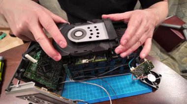 Parçalanmış bir CD oynatıcının iç mekanizması üzerinde çalışan ellerin yakın plan görüntüsü, açık devre kartları ve bir tablo üzerindeki onarımlar sırasında bileşenleri ile birlikte.