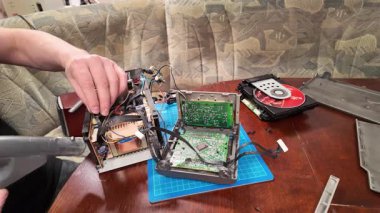  Bir adam devre kartı ve elektronik üzerinde çalışırken parçalanmış bir CD çaların iç bileşenlerini temizlemek için elektrikli süpürge kullanır.