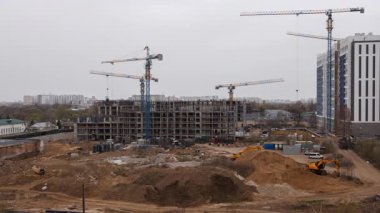 Apartman inşaatının zamanı, vincin dönmesi, araçların hareket etmesi ve çalışanların aktif olması, hızlı kentsel gelişim ve mühendislik ilerlemelerini gösteriyor