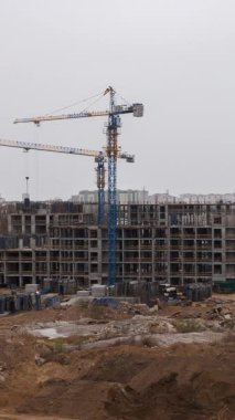 Dikey zaman dilimi videosu bina inşaatını mavi kule vinçleriyle kaydediyor. Kentsel kalkınma alanındaki beton yapı yükselirken işçiler katlar boyunca hareket ediyorlar.