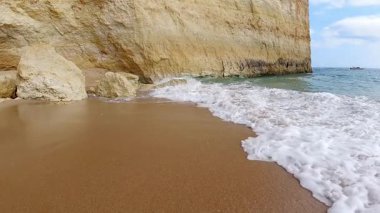 Görkemli altın kireçtaşı kayalıklarının el değmemiş kumsalla buluştuğu sakin kıyı manzarası. Yumuşak dalgalar, yüksek doğal kaya oluşumlarının altındaki kıyı şeridini okşarken narin beyaz köpük oluşturur.