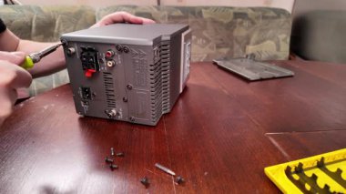 Tornavida kullanılarak ahşap bir masaya dikkatlice sökülen bir stereo cihaz. Görünür vidalar ve bileşenler tamir işlemini ve elektronik bakım işini vurgular
