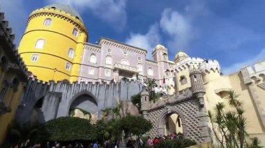 Lizbon, Portekiz - 14 Ekim 2019: Portekiz 'in Sintra kentindeki canlı sarı ve pembe Pena Sarayı' na girmek için kuyrukta bekleyen turistler, kendine özgü kuleleri ve romantik mimarisi ile dağınık mavi bulutlu parlak bir gökyüzüne karşı kurulmuştur.