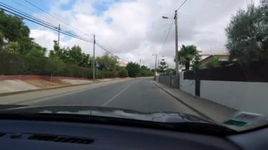 Hareket halindeki araba penceresinden manzaralı manzarayı yakalayan ilk kişi geleneksel beyaz evler, taş duvarlar ve parçalı bulutlu gökyüzü altındaki yemyeşil Akdeniz bitkileri ile Portekiz 'in huzurlu meskûn mahallelerinden geçiyor.