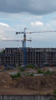 Bulutlu bir arka plan karşısında durağan mavi vinçlerin ve bitmemiş konut binalarının yer aldığı bir inşaat alanının dikey zaman çizelgesi, kentsel gelişim ve inşaat endüstrisinin gerçek zamanlı ilerlemesini gösteriyor