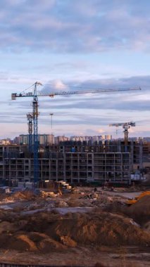 İkamet planının dikey zaman çizelgesi. İnşaat vinçlerinin bulutlara karşı durduğu altın gece ışığıyla aydınlatılıyor. Yatırım fırsatı görselleştirmesi modern apartman kompleksi inşaatı ve kentsel genişlemeyi yakalıyor